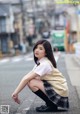 A woman in a school uniform crouching down on the street.