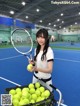 A woman holding a tennis racket and a basket of tennis balls.