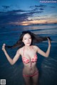 A woman in a red bikini standing in the ocean.